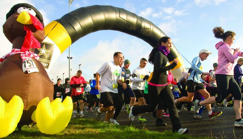 giant inflatable turkey marking the start of a turkey trot Thanksgiving race, with runners taking off (Boston turkey trots)