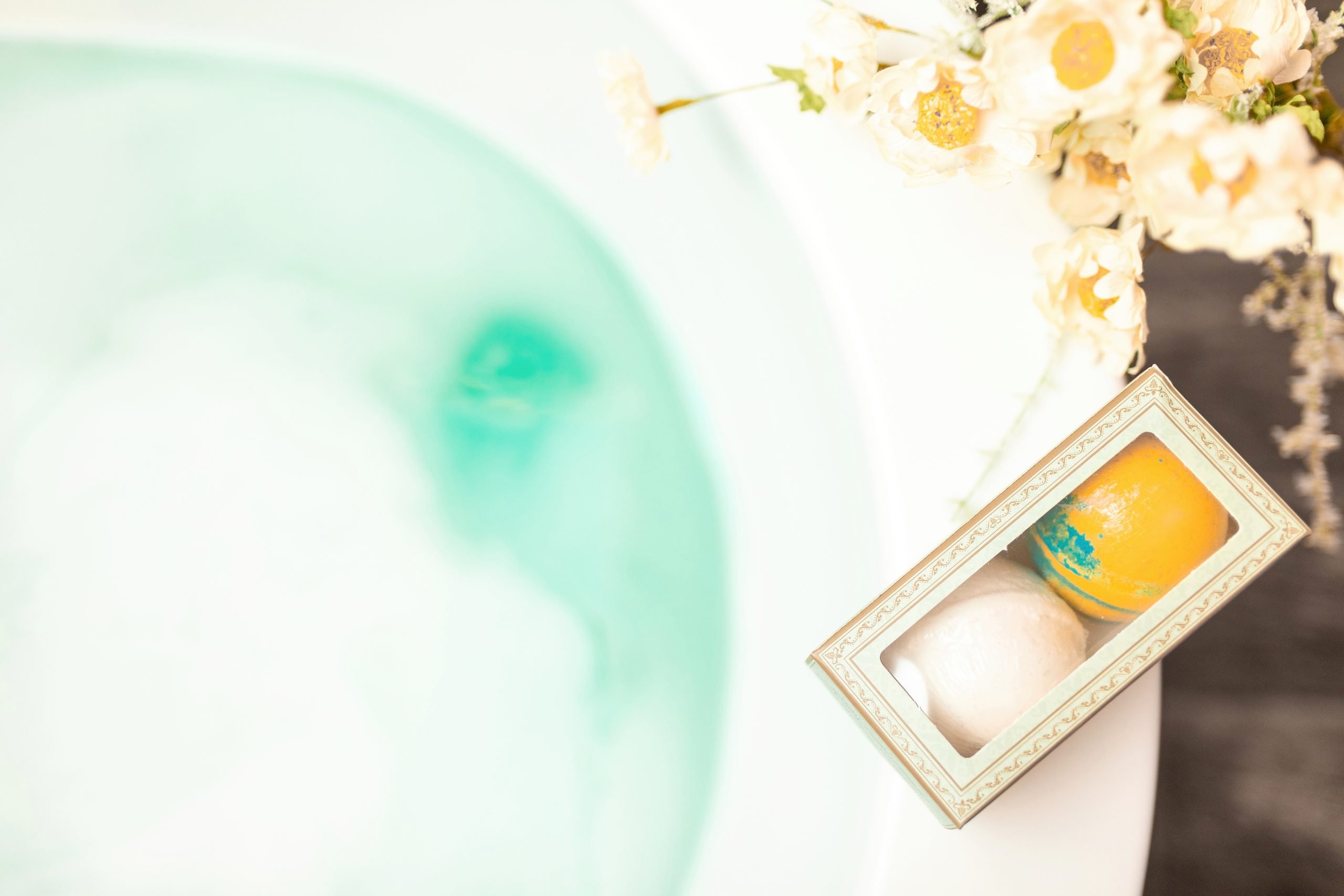 Mom Bomb bath bombs sitting on the edge of a filled bathtub
