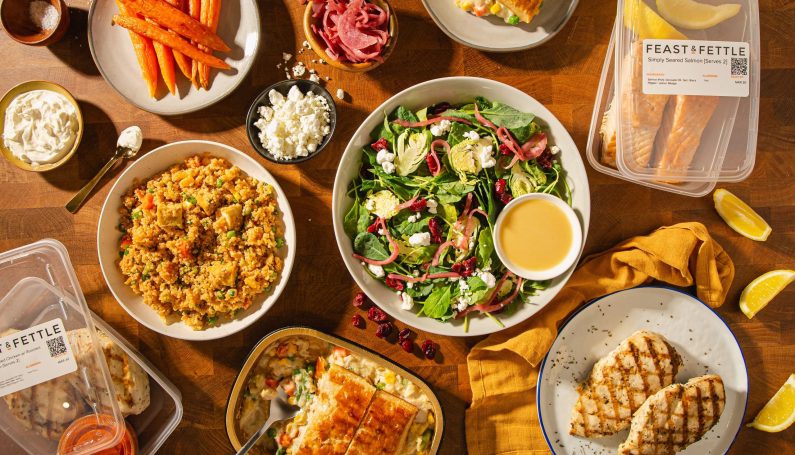 Salad, grilled chicken, carrots, and various other plates and bowls of food on a wooden table.