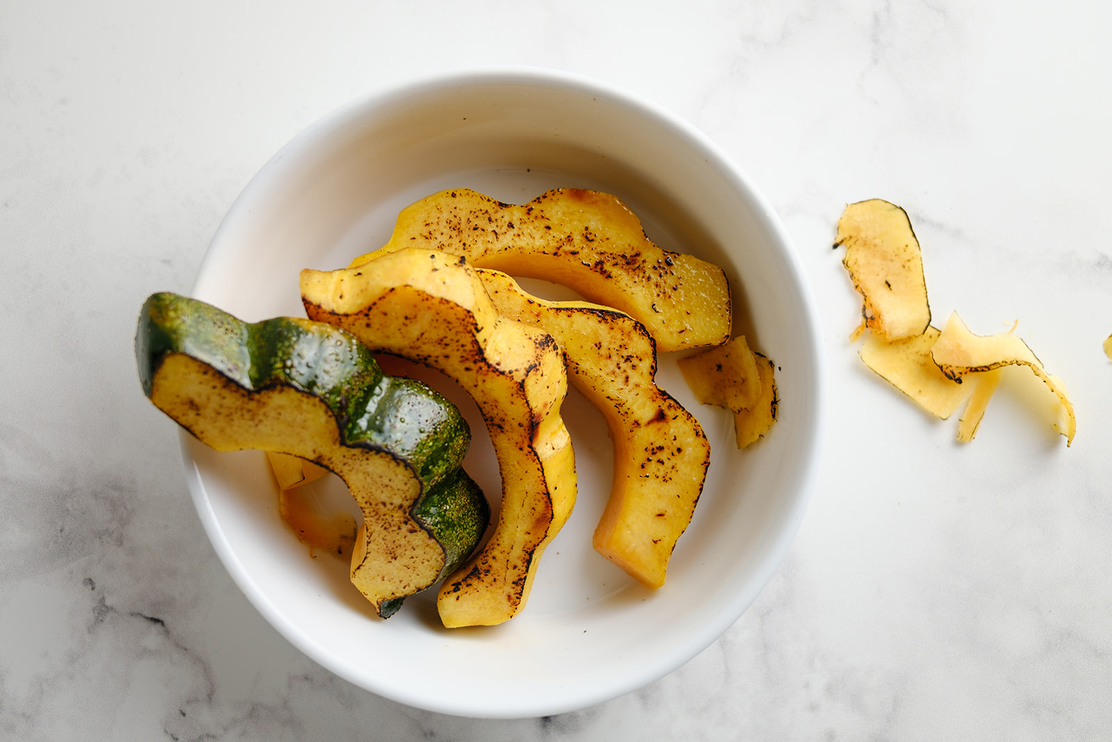 roasted and seasoned slices of acorn squash in a white bowl on a countertop