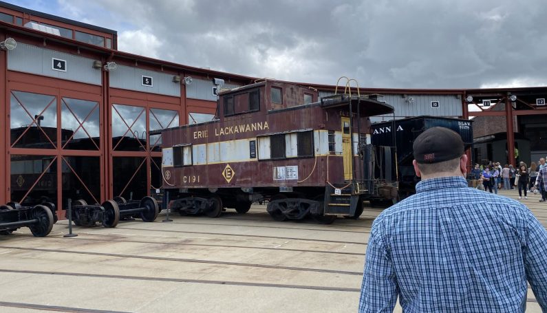 Walking through the train yard at Steamtown in Scranton, PA. An Erie Lackawanna caboose is outside of a train shed.
