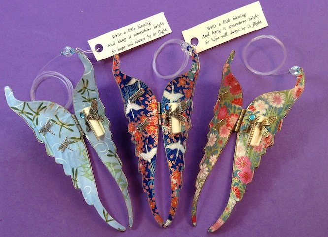 Three metal butterflies adored with colorful floral designs and paper messages attached to them.