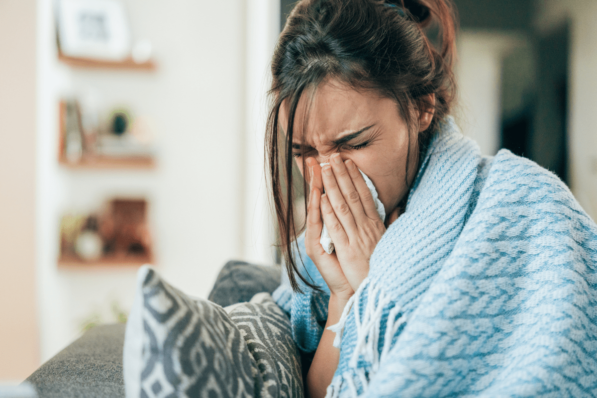 woman blowing her nose, feeling sick, showing how moms don't get sick days