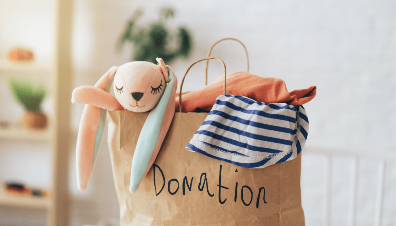 Paper bag with the word donation written on it. Clothes and stuffed animal bunny are coming from the top of the bag.