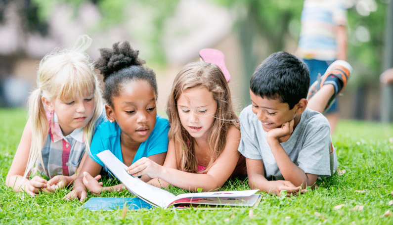 four children laying on the grass reading together (books with Black characters, books to celebrate Black History Month)