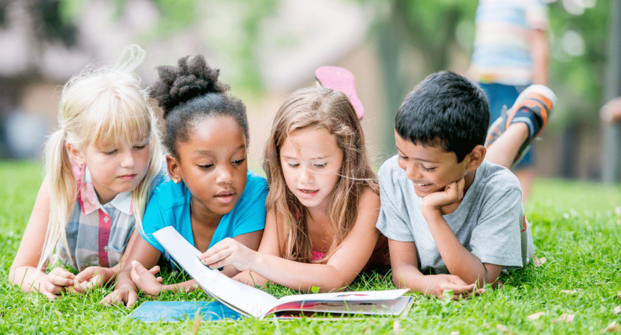 four children laying on the grass reading together (books with Black characters, books to celebrate Black History Month)