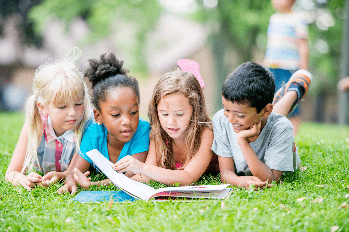 four children laying on the grass reading together (books with Black characters, books to celebrate Black History Month)