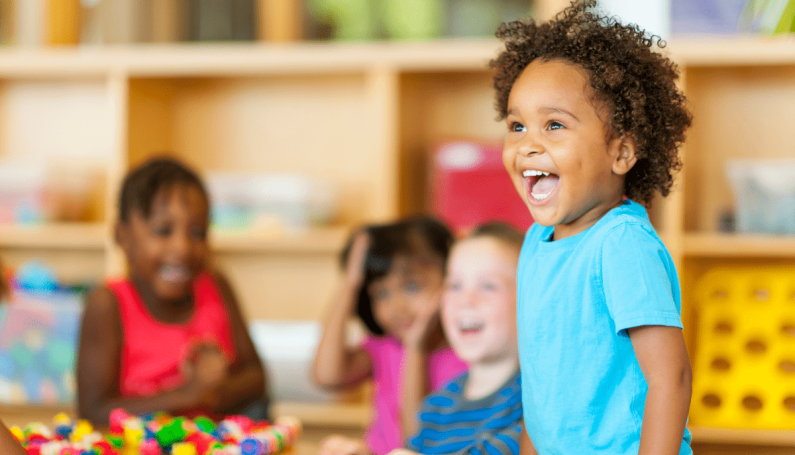 smiling child at preschool surrounded by a table full of friends