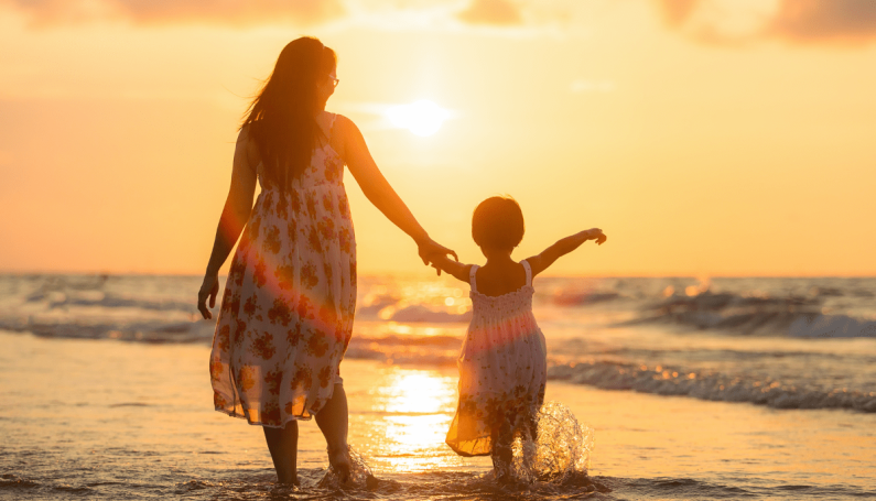 mother and child standing in the shallow waves at the beach