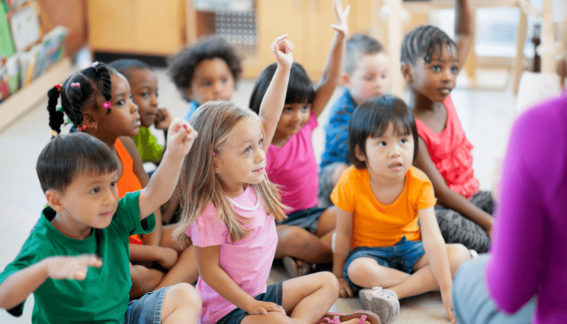 preschool children sitting on floor raising hands