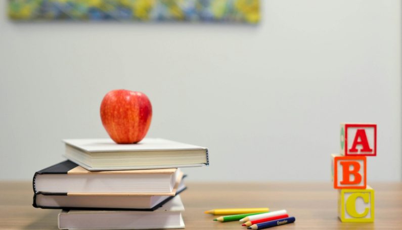 apple sitting on stack of book's on school desk (5 questions to ask at child's parent-teacher conference)