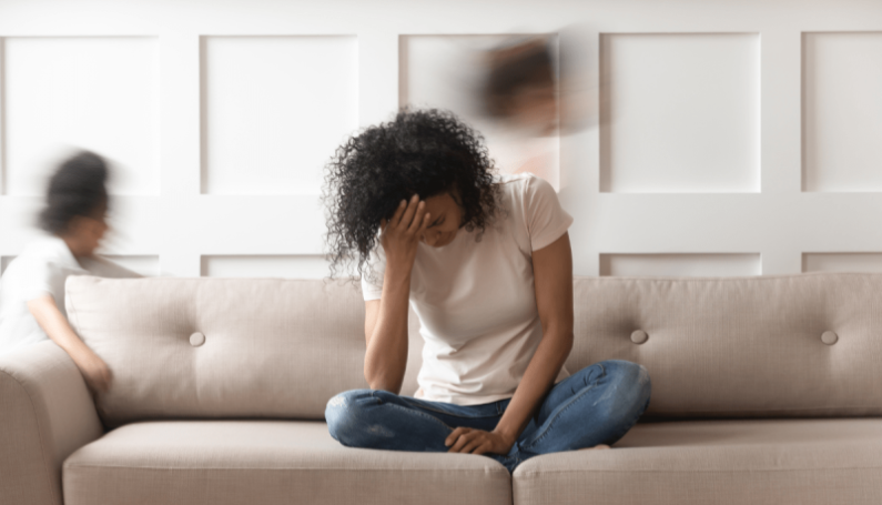 tired mom sitting on couch with children running around her