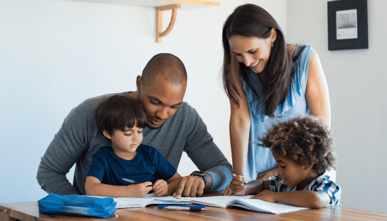 parents and two children gathered around a table with books and pencils (family language learning/immersion)