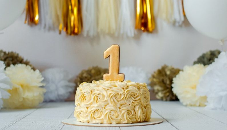 birthday cake with number one candle in front of metallic streamers (non-toy gifts for 1-year-old for first birthday)