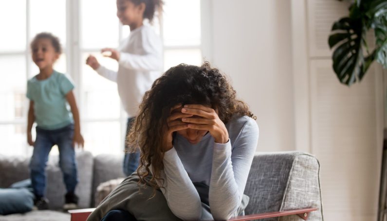 stressed mother with two children playing busily nearby (U.S. surgeon general warning about parents and stress)