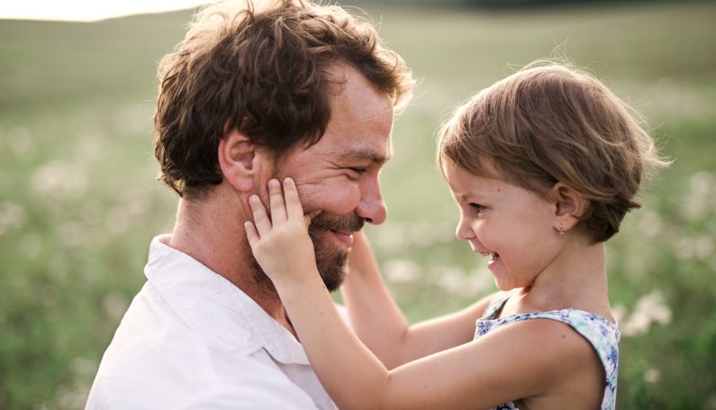 Young father in green sunny summer nature holding cute daughter in his arms (men's mental health, Reset Health)