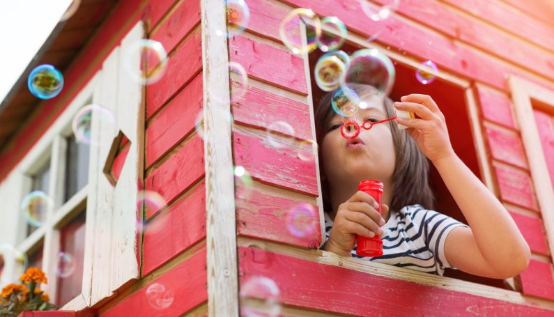 child inside a backyard playhouse (backyard structure ideas for kids)