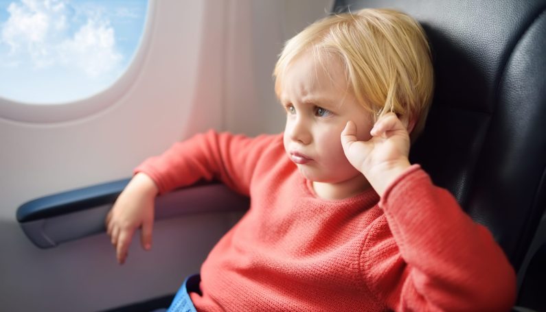young boy sitting in airplane window seat (airplane travel with kids, tantrum)