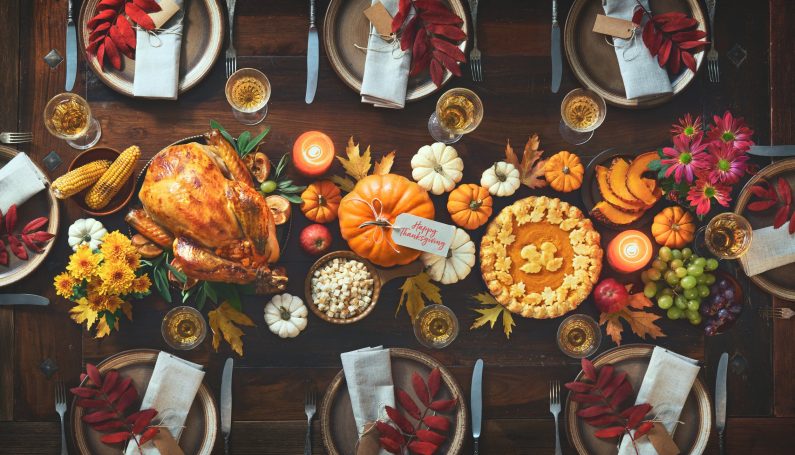 Thanksgiving celebration traditional dinner. Roasted turkey garnished with cranberries on a rustic style table decorated with pumpkins, vegetables, pie, flowers and candles. Thanksgiving meal to go from Boston restaurant
