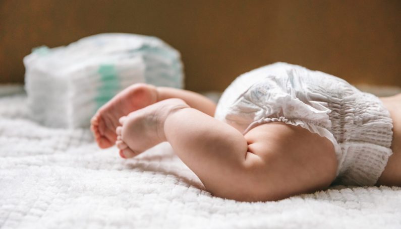 A baby in a diaper with a stack of diapers (where to donate diapers in Boston, diaper banks)
