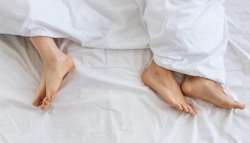 woman and man's feet in bed far from each other (10 reasons moms aren't getting busy, sex)