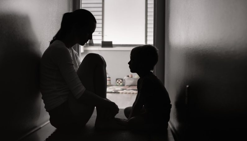 Mother and son sitting on the floor at home in the dark (school shooting)