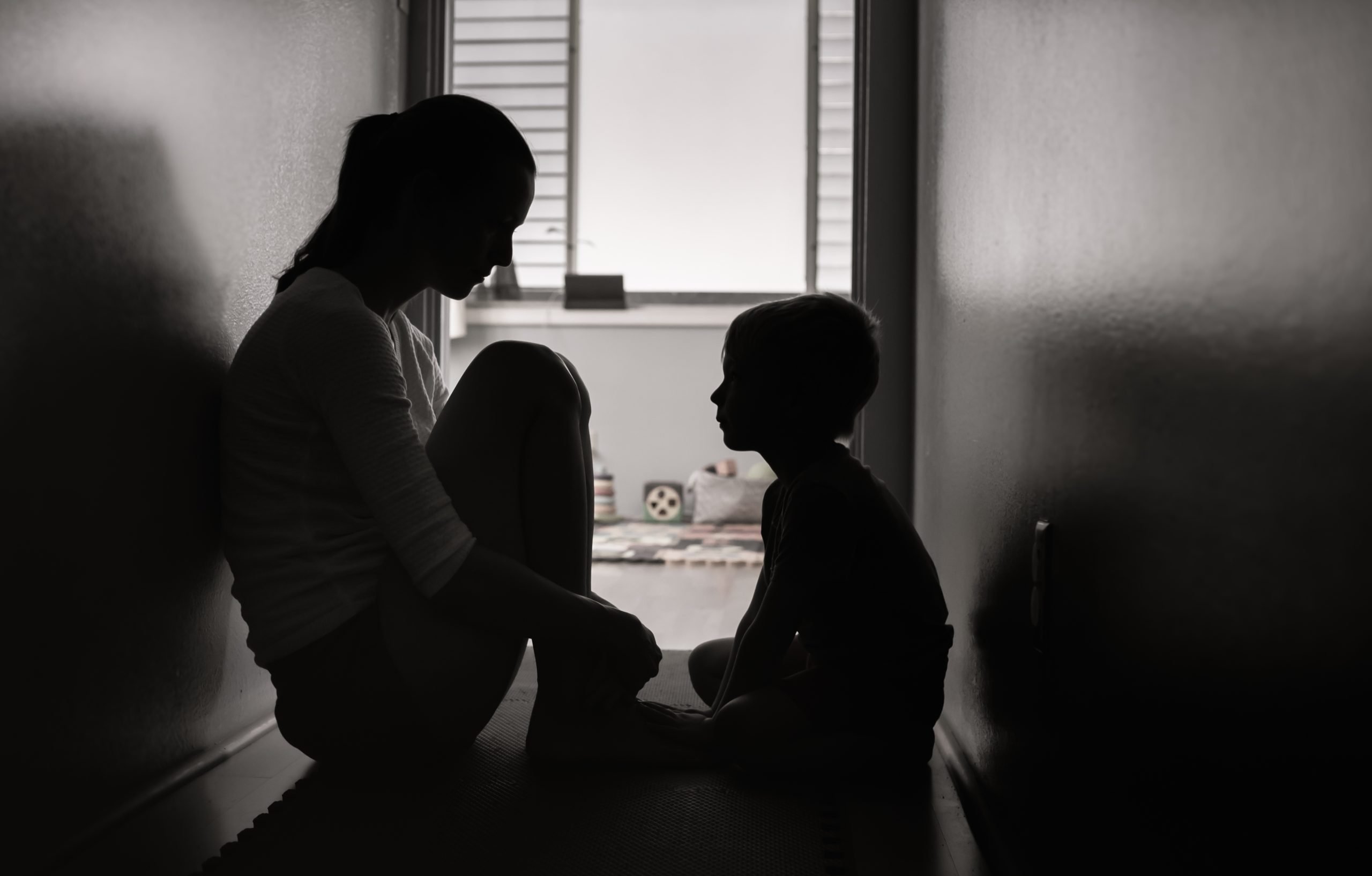 Mother and son sitting on the floor at home in the dark (school shooting)
