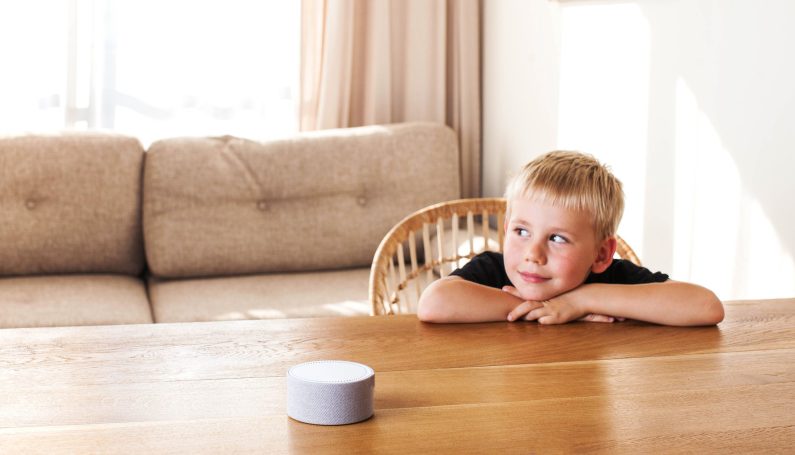 Cute boy sitting at the dining table and listening to the smart speaker. (Alexa Skills for kids)