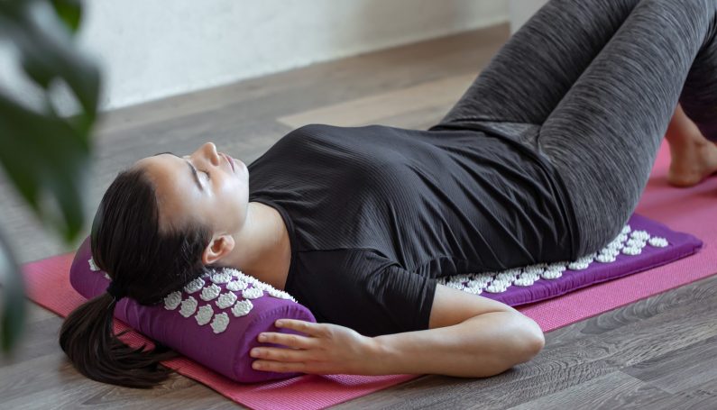 A woman lies on a purple acupuncture massage pillow and a mat with white massage tips. (mom back, acupressure mat for women)
