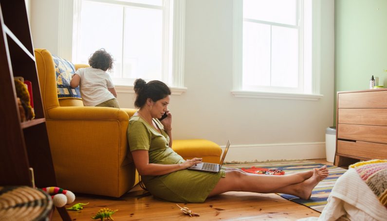 working mom taking a phone call while on a laptop computer in son's playroom