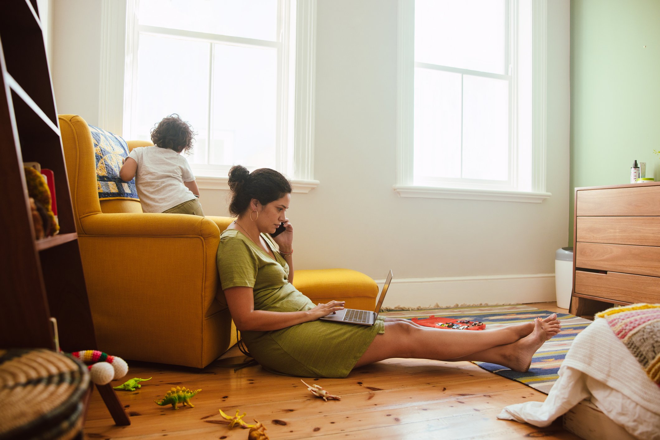 working mom taking a phone call while on a laptop computer in son's playroom