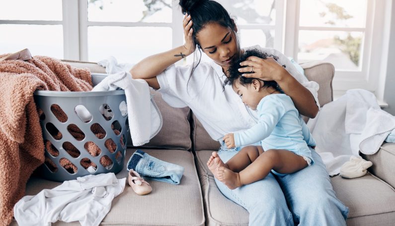 mom with clingy baby on lap surrounded by laundry (stress relief tips for moms)