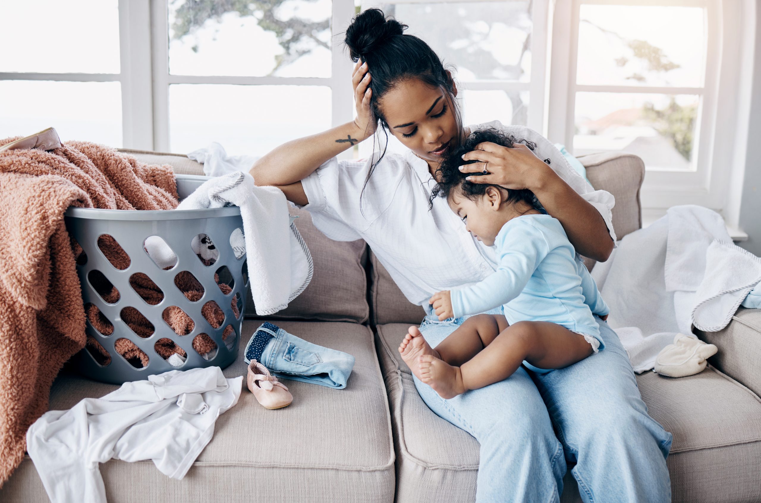 mom with clingy baby on lap surrounded by laundry (stress relief tips for moms)