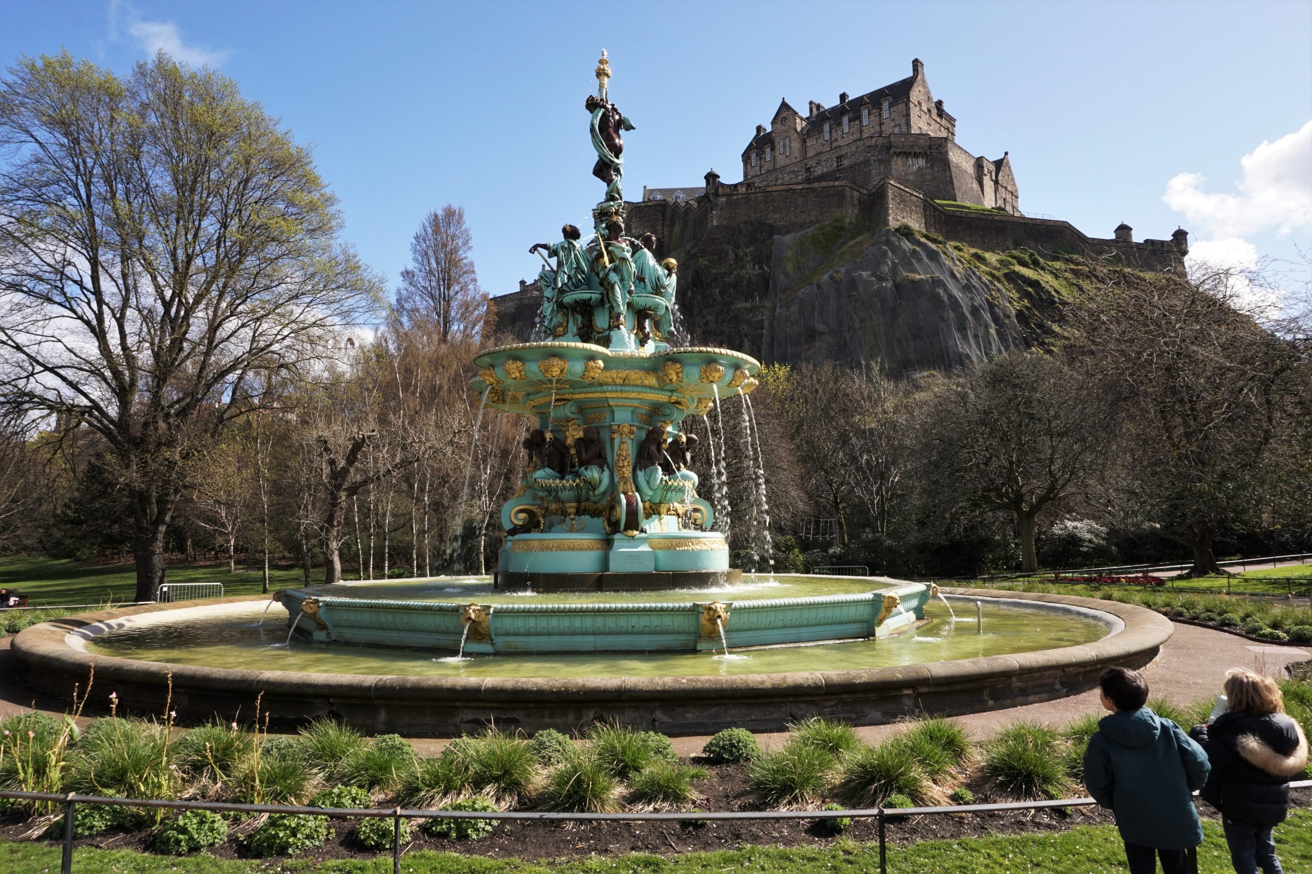 Edinburgh, Scotland, children looking at the Ross Fountain in Princes Street Gardens on a sunny spring day. Edinburgh Castle is in the background. (Europe, Scotland with kids)