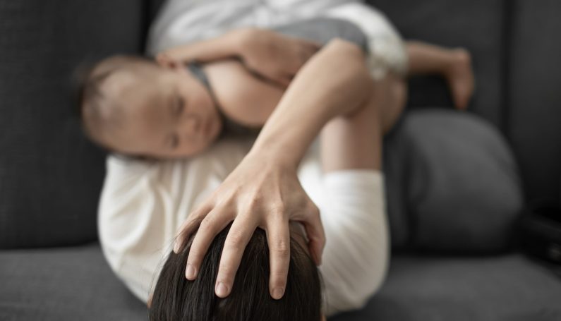mother with baby in arms, headache, multi-tasking (tired mom)