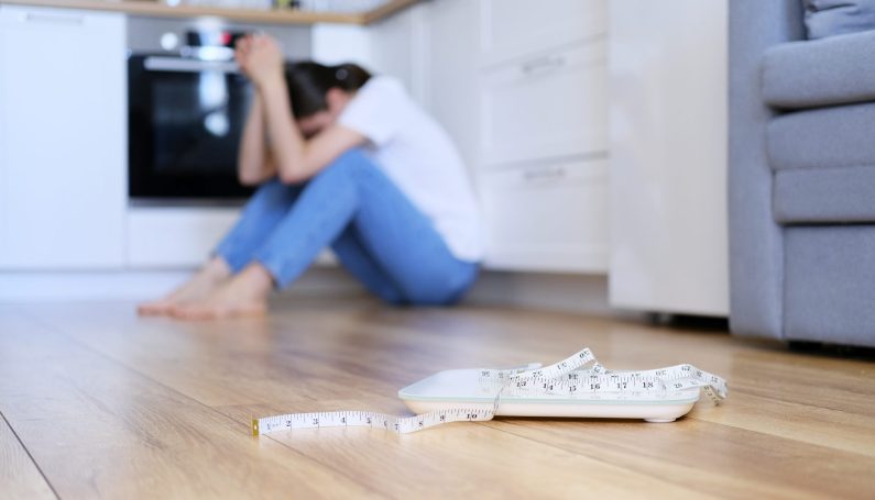 disappointed woman near scale and measuring tape (eating disorder, anorexia in women and moms)