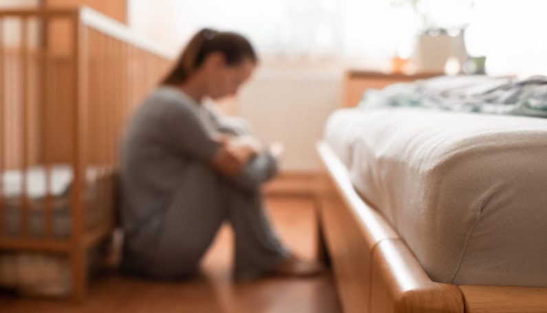 woman with postpartum depression sitting by empty crib