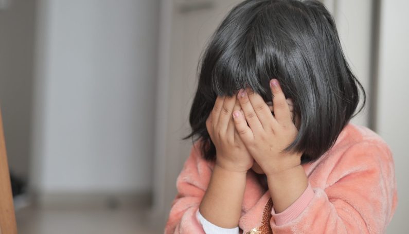 an upset child covers her face with her hands (teaching kids about making mistakes)