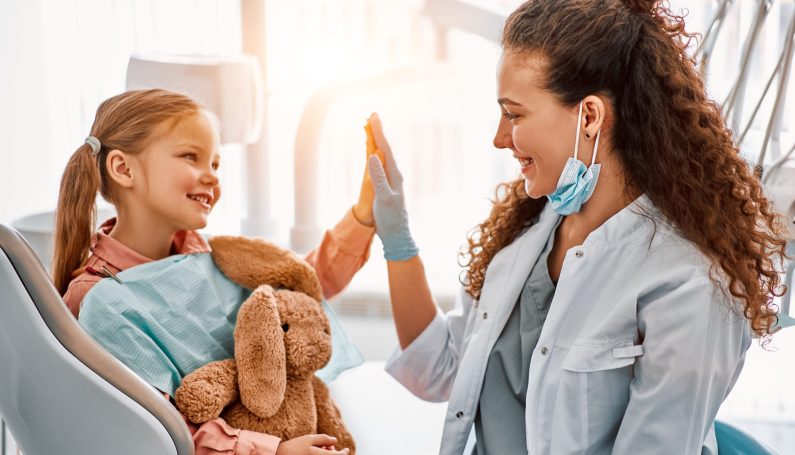 little girl sitting in dentist chair, giving high five to female doctor and laughing. (pediatric dentist, it's OK to break up with your dentist)