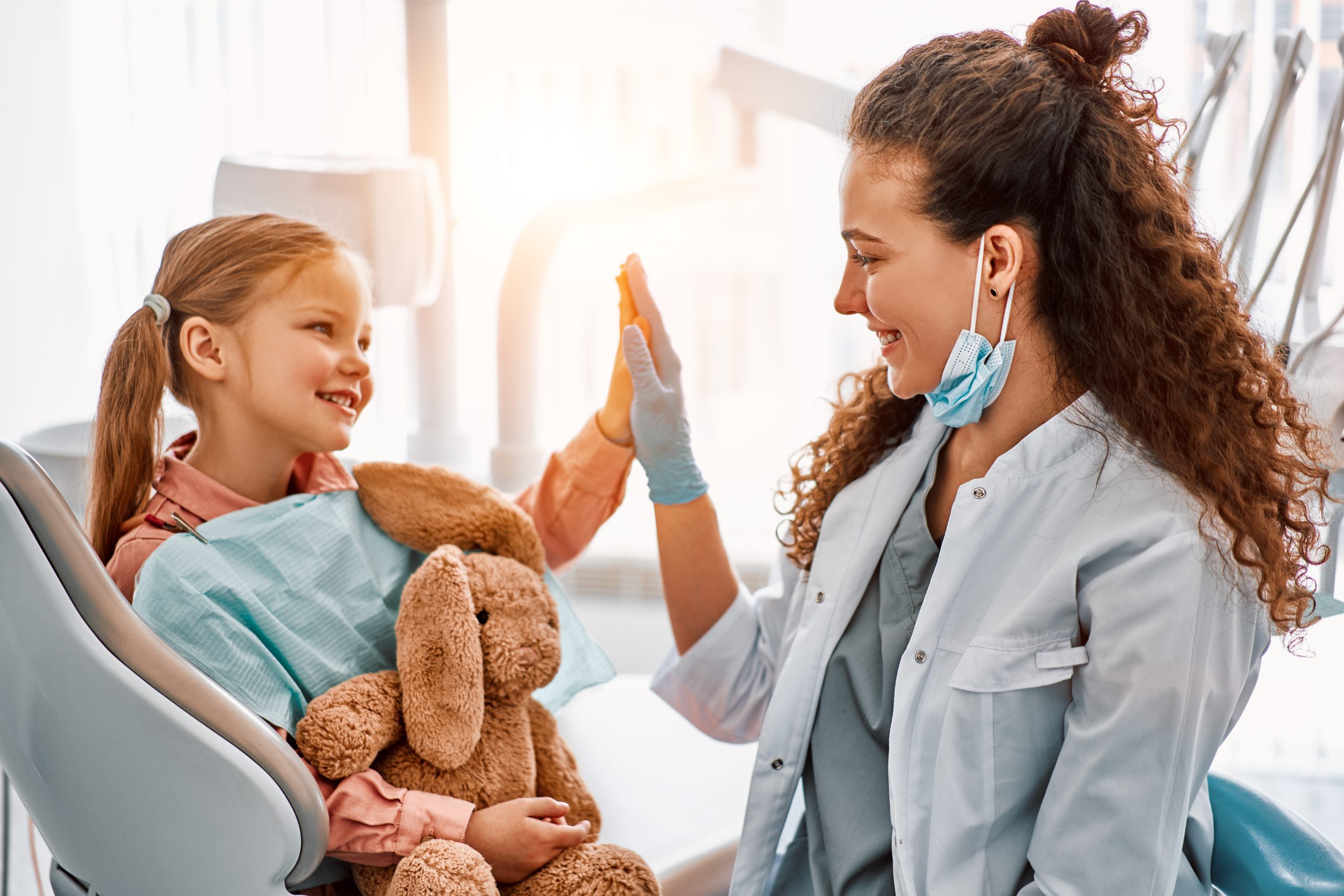 little girl sitting in dentist chair, giving high five to female doctor and laughing. (pediatric dentist, it's OK to break up with your dentist)