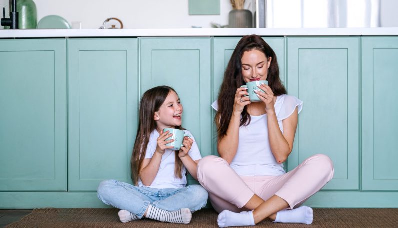 mother sitting on kitchen floor with daughter, drinking coffee (mom uniform)