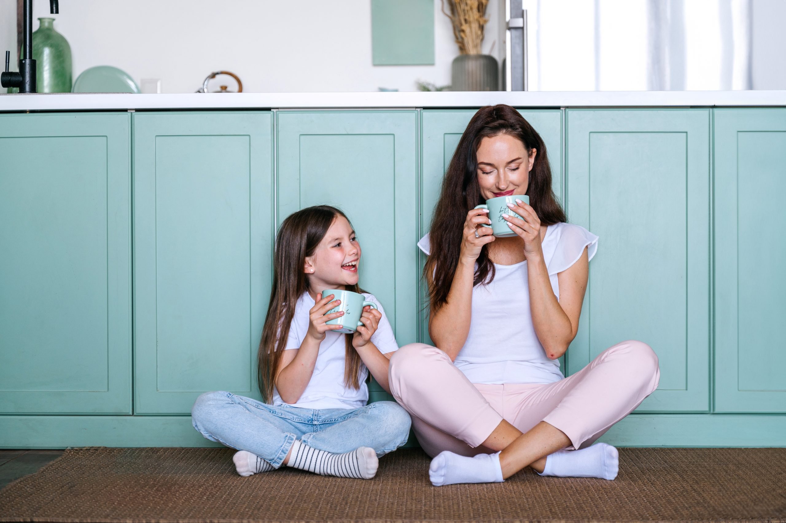 mother sitting on kitchen floor with daughter, drinking coffee (mom uniform)