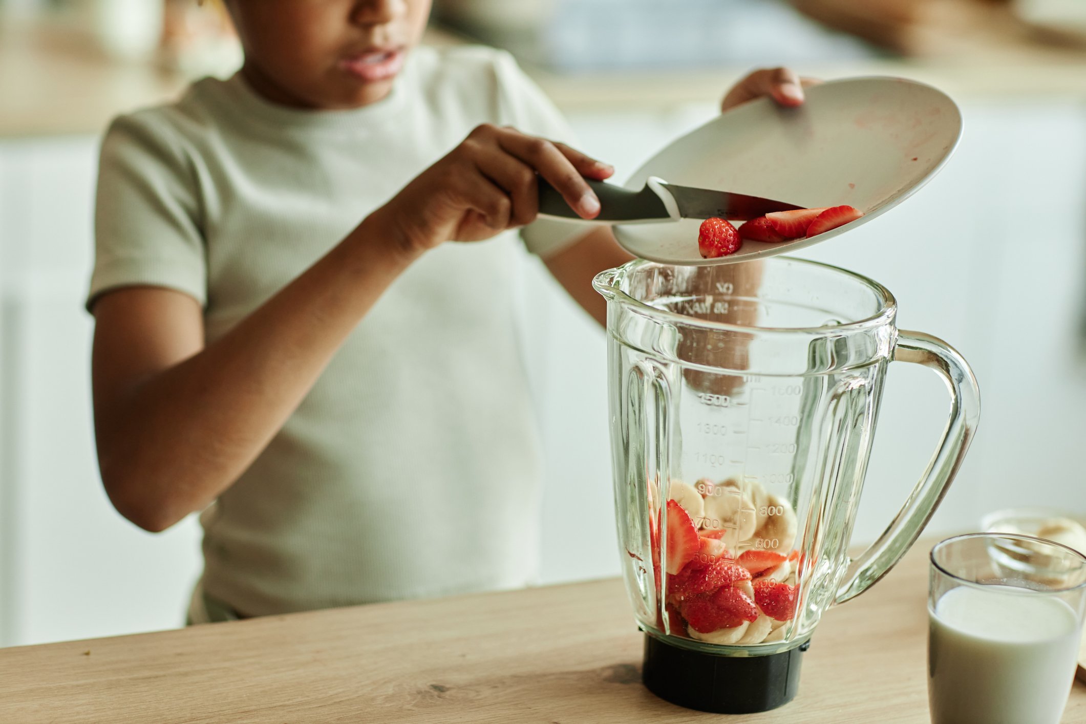 little girl carefully adding strawberries to blender making fruit smoothie with banana (snacks kids can make on their own)