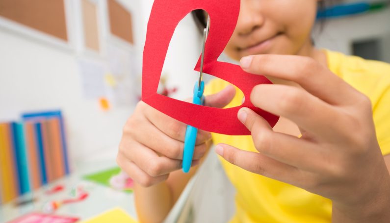 girl cutting out paper heart for class valentines at school