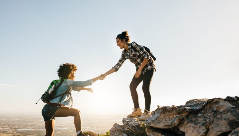 Young woman helping friend climb up a rock (making mom friends)