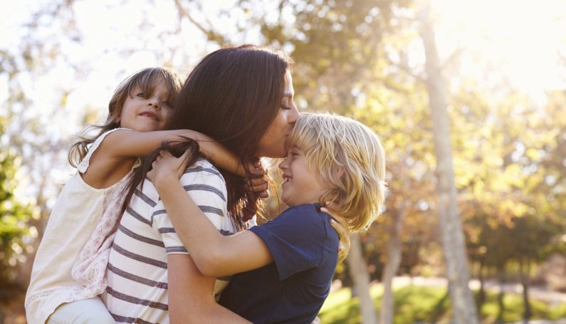mother carrying son and daughter as they play in the park (parenting styles)