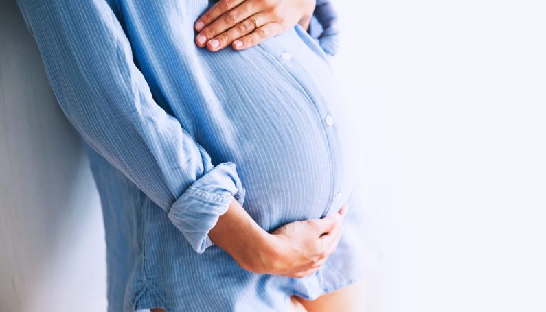 Pregnant woman holds hands on belly (maternity clothing for petite or short women)