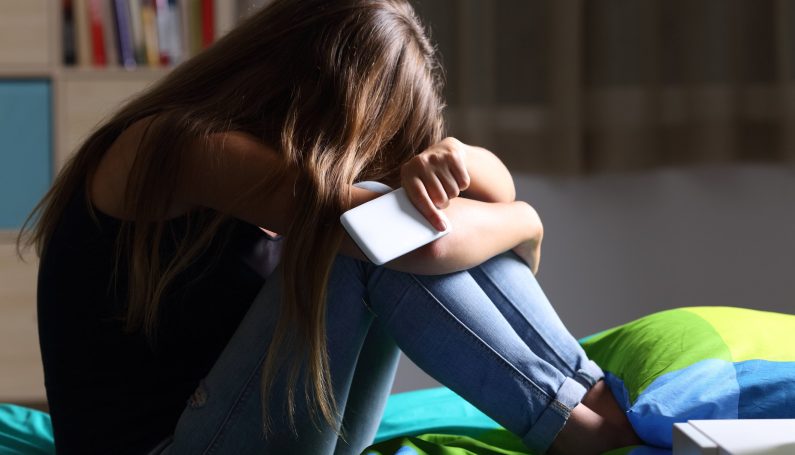 sad teen sitting on a bed holding a phone (teenager stress)