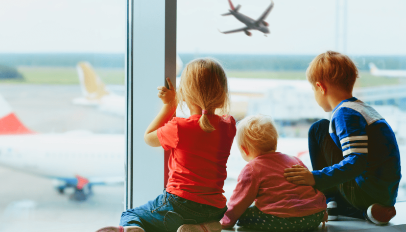 three children watching airplanes from inside an airport, international travel with kids