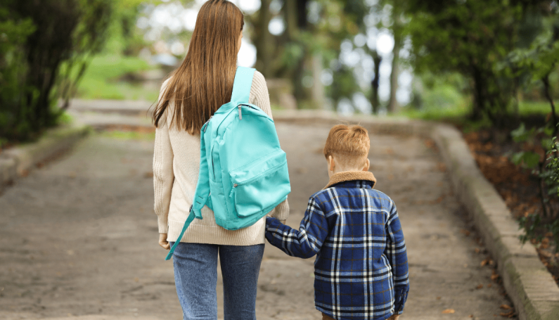 mom with backpack holding hands with school-aged child (kindergarten and working mom)